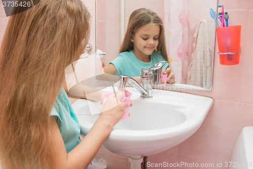 Image of The girl pours in a cup of warm water to rinse your mouth