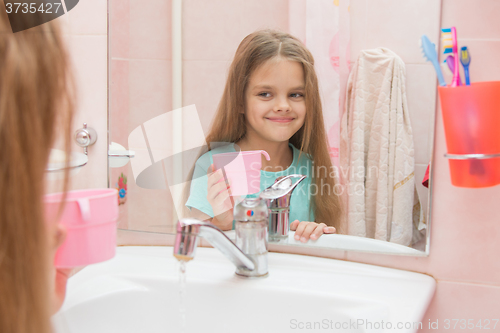 Image of Happy girl holding a cup and looks in the mirror in the bathroom