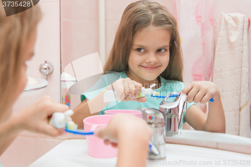 Image of Happy little girl squeezes the toothpaste from a tube on toothbrush