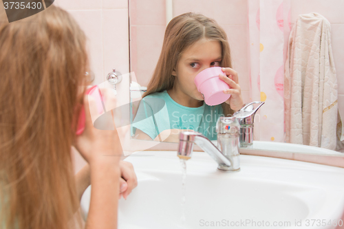 Image of Girl dials the water in the mouth from the cup by rinsing the mouth after brushing