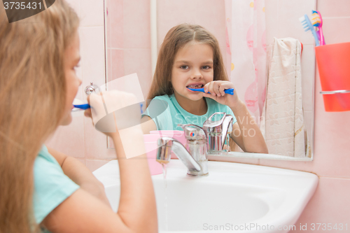 Image of Six year old girl cleans teeth side looking in the mirror in the bathroom