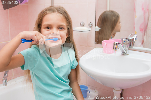 Image of Six year old girl brushing her teeth and turned away from the sink looks in the picture