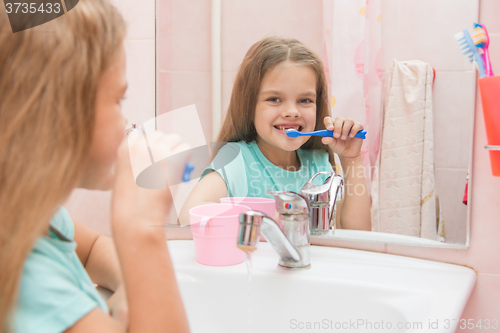 Image of Six year old girl brushing the front teeth with a smile and looked into the frame