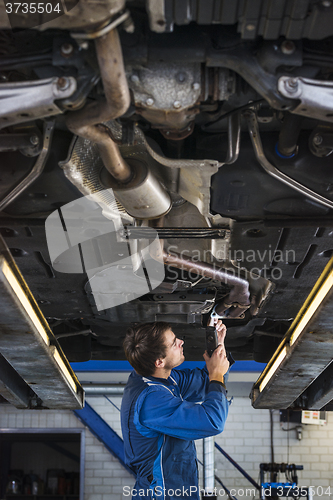 Image of Young mechanic repairing the exhaust of a car