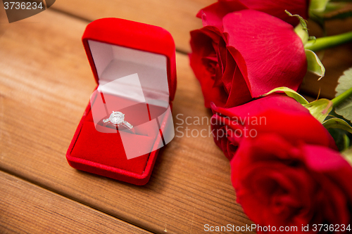 Image of close up of diamond engagement ring and red roses