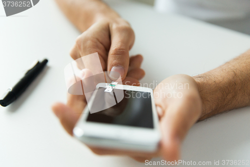 Image of close up of man with smartphone making blood test