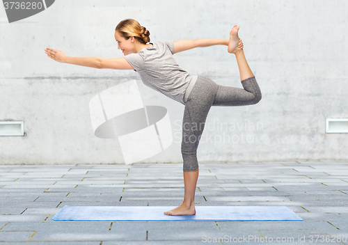 Image of woman making yoga in lord of the dance pose on mat