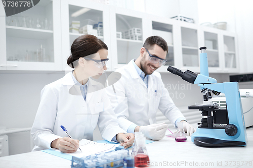 Image of scientists with clipboard and microscope in lab