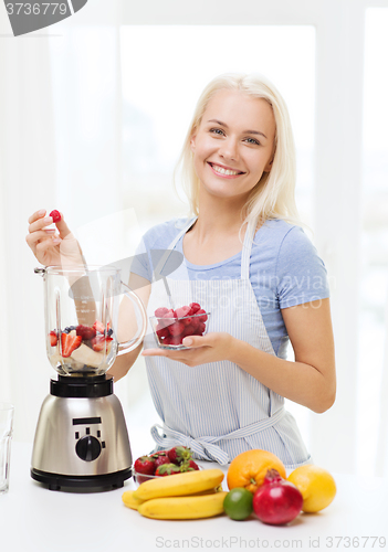 Image of smiling woman with blender preparing shake at home