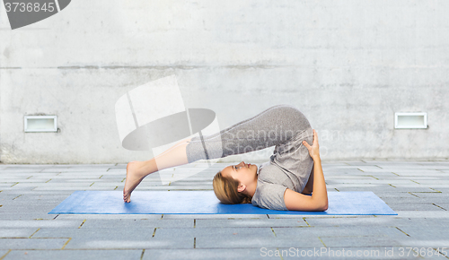 Image of woman making yoga in plow pose on mat outdoors