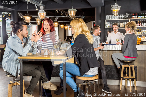 Image of Friends Conversing While Sitting At Table In Bar