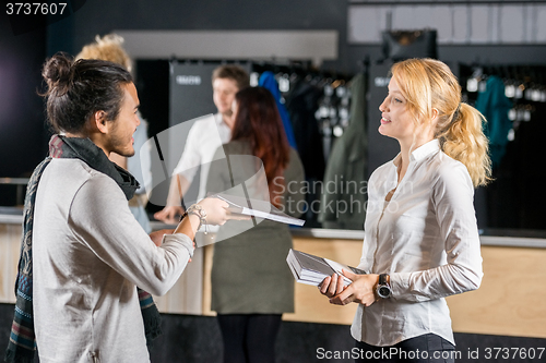 Image of Man Giving Book To Friend By Bag Deposit Counter