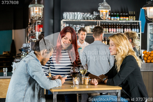 Image of Women Looking At Friend Using Mobile Phone In Bar