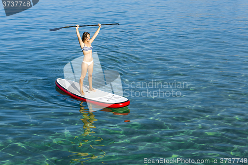 Image of A beautiful and happy woman with arms up and learning paddle-sur