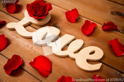 Image of close up of word love cutout with red rose on wood