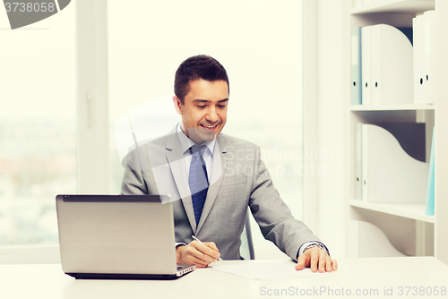 Image of smiling businessman with laptop and papers