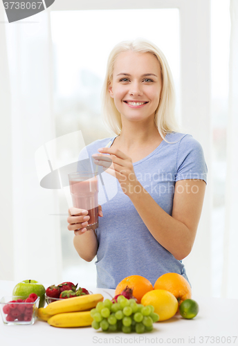 Image of smiling woman drinking fruit shake at home