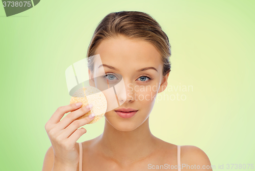 Image of young woman cleaning face with exfoliating sponge