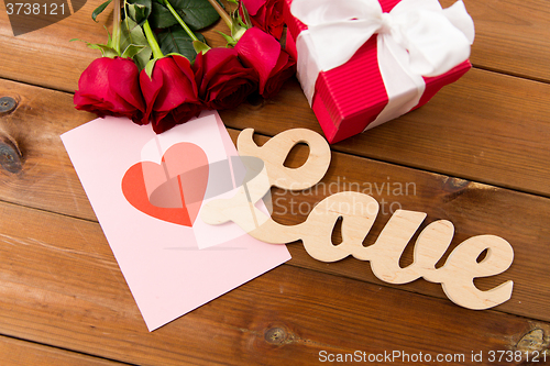 Image of close up of gift box, red roses and greeting card