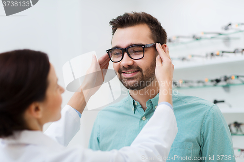 Image of optician putting on glasses to man at optics store