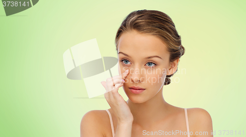 Image of young woman applying cream to her face over green
