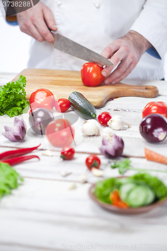 Image of Chef cutting a red tomato his kitchen