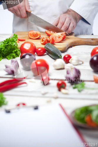 Image of Chef cutting a red tomato his kitchen
