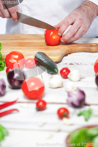 Image of Chef cutting a red tomato his kitchen