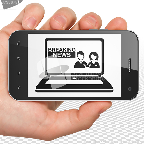 Image of News concept: Hand Holding Smartphone with Breaking News On Laptop on display