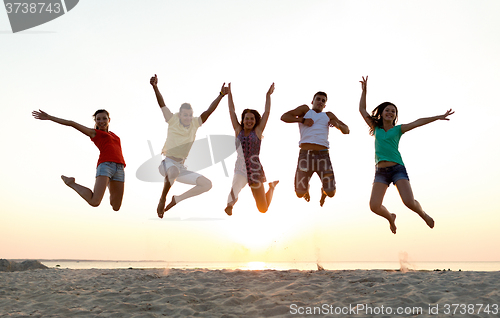 Image of smiling friends dancing and jumping on beach