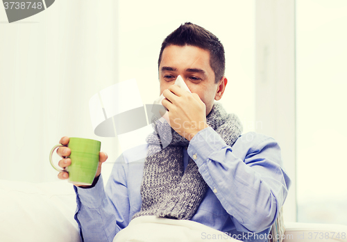 Image of ill man with flu drinking tea and blowing nose