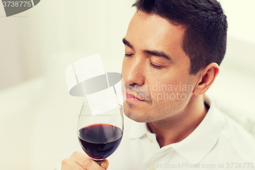 Image of happy man drinking red wine from glass at home