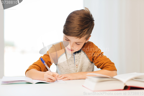 Image of smiling student boy writing to notebook at home