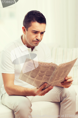 Image of sad man reading newspaper at home