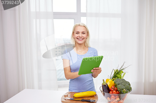 Image of smiling young woman with tablet pc cooking at home