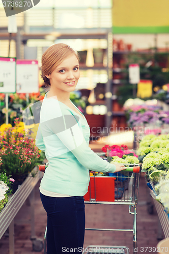 Image of happy woman with shopping trollye buying flowers