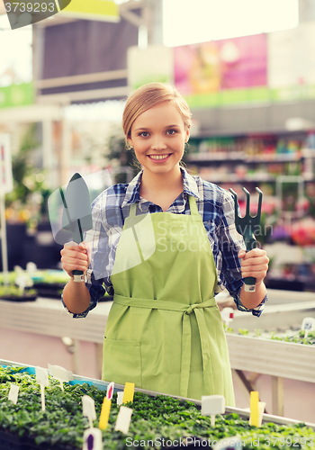 Image of happy woman with gardening tools in greenhouse