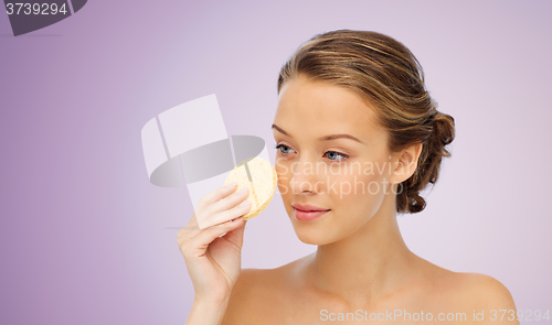 Image of young woman cleaning face with exfoliating sponge