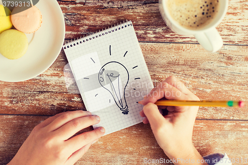 Image of close up of hands drawing bulb to notebook