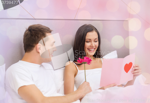 Image of happy couple in bed with postcard and flower