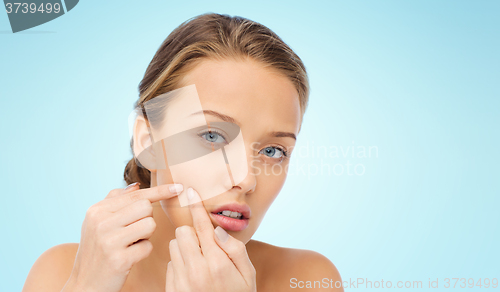 Image of young woman squeezing pimple on her face