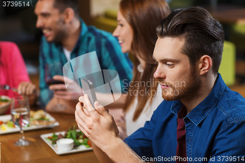 Image of man with smartphone and friends at restaurant