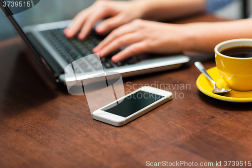 Image of close up of smartphone and hands typing on laptop