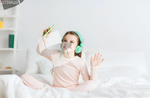 Image of girl sitting on bed with smartphone and headphones