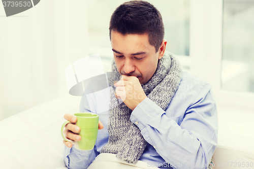 Image of ill man with flu drinking tea and coughing at home