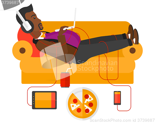 Image of Man with gadgets lying on sofa.