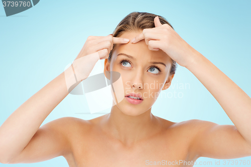 Image of young woman squeezing pimple on her face
