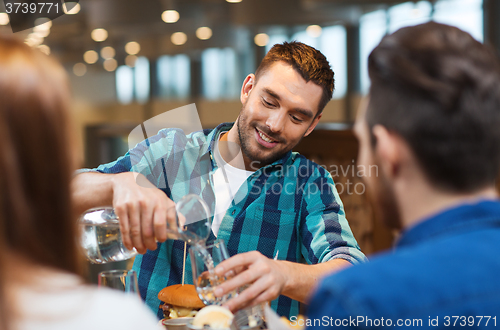 Image of happy man with friends pouring water at restaurant