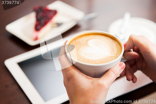 Image of close up of hands with coffee, tablet pc and cake