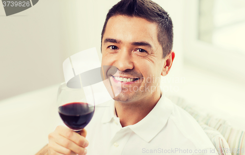 Image of happy man drinking red wine from glass at home